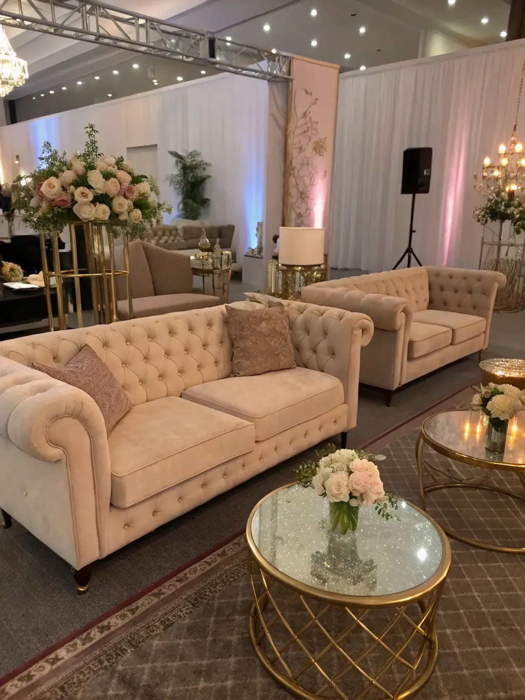 A plush, modern beige velvet sofa with gold accents, set in a chic lounge area with floral arrangements and ambient lighting, ideal for upscale gatherings and weddings.